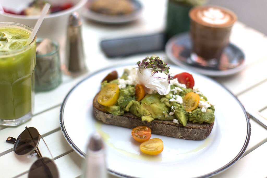 An avocado smash on a plate with a poached egg and tomatoes.