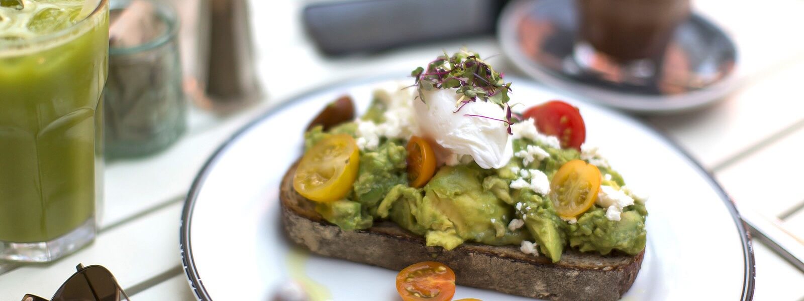 An avocado smash on a plate with a poached egg and tomatoes.