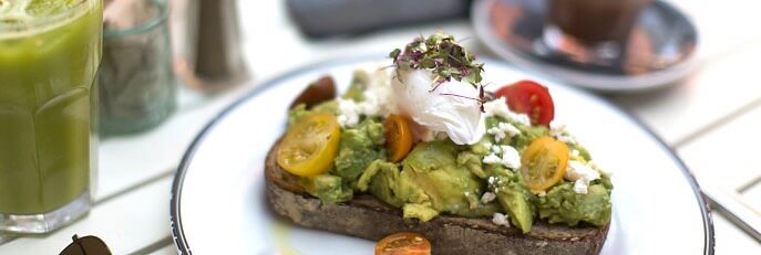 An avocado smash on a plate with a poached egg and tomatoes.