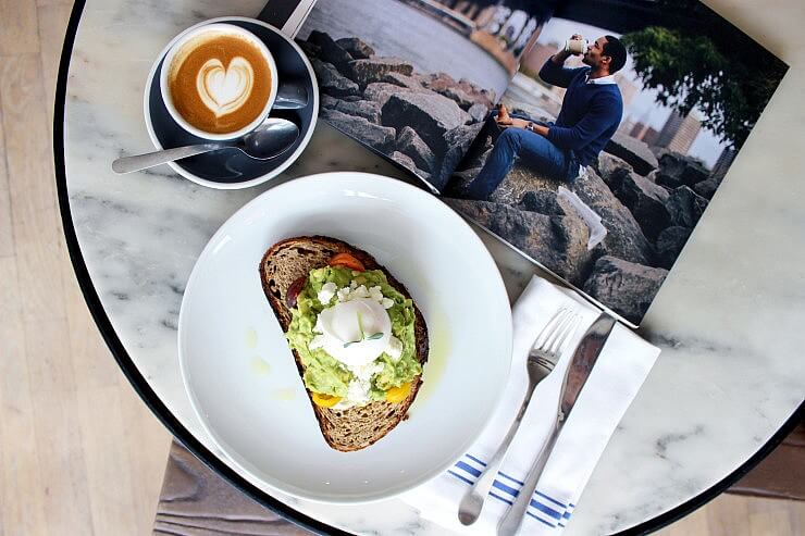 aerial shot of an avocado smash with a flat white and an open magazine. 