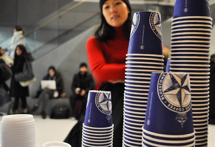 4 stacks of Bluestone Lane cups with people in the background. 