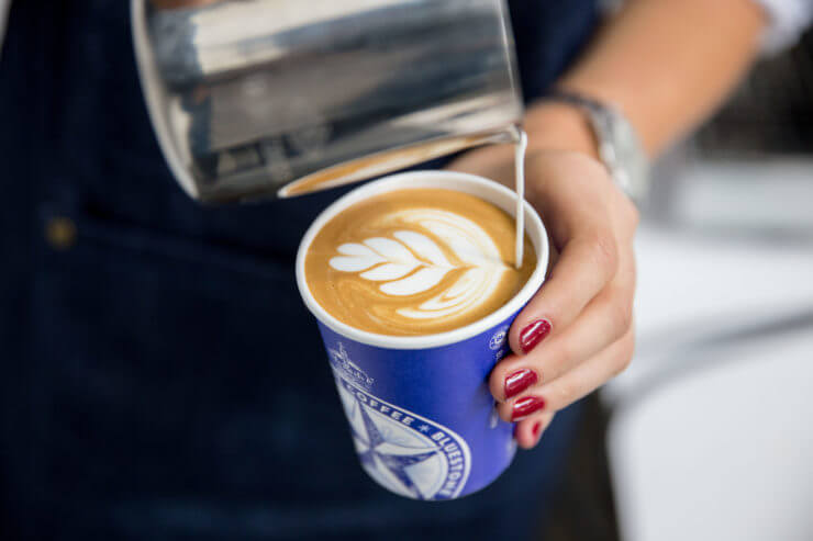 Barista pouring latte art into a bluestone lane cup. 