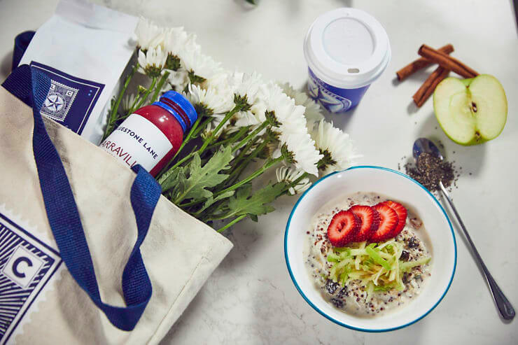 Bircher Muesli served with fruit next to a Bluestone Lane tote bag filled with flowers. 