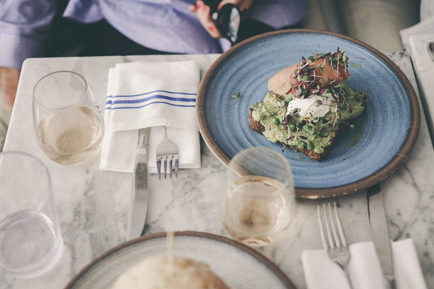 Table top at Bluestone Lane with white wine and an Avo Smash with an egg and smoked salmon. 