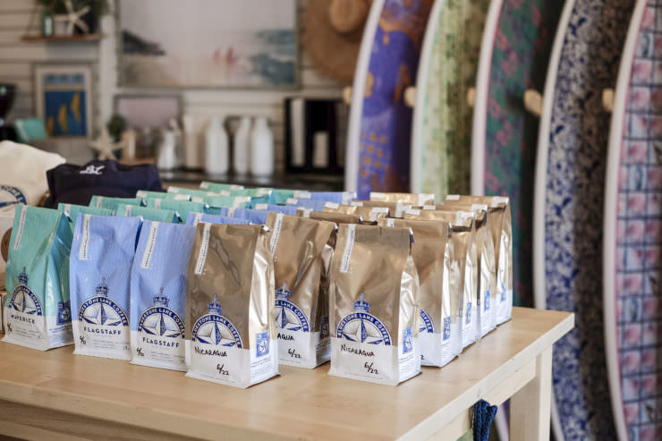 Bluestone Lane retail coffee bags on a table in the Montauk store with custom surf boards in the background. 