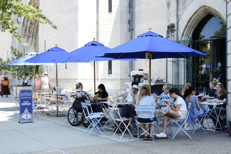 Outside of Bluestone Lane Upper East Side with outdoor seating and blue umbrellas. 