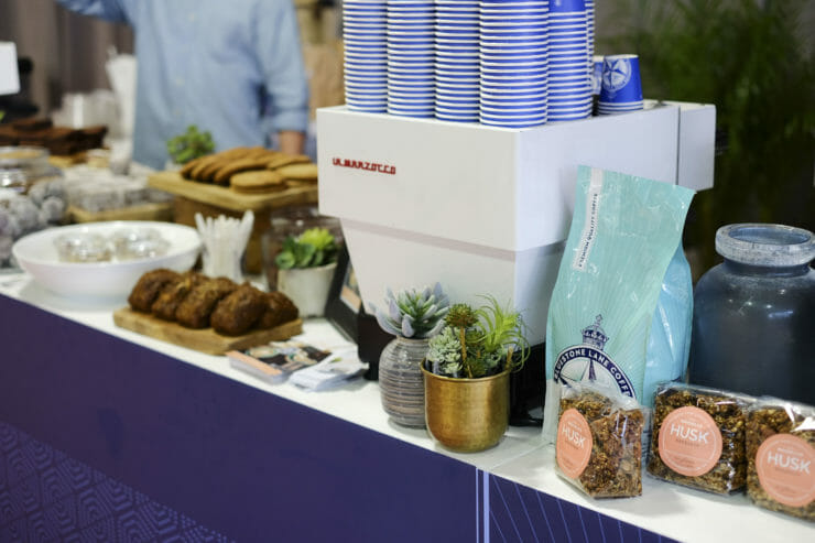mini la marzocco coffee machine on table surrounded by mini plant decorations, pastries and little bags on granola. 