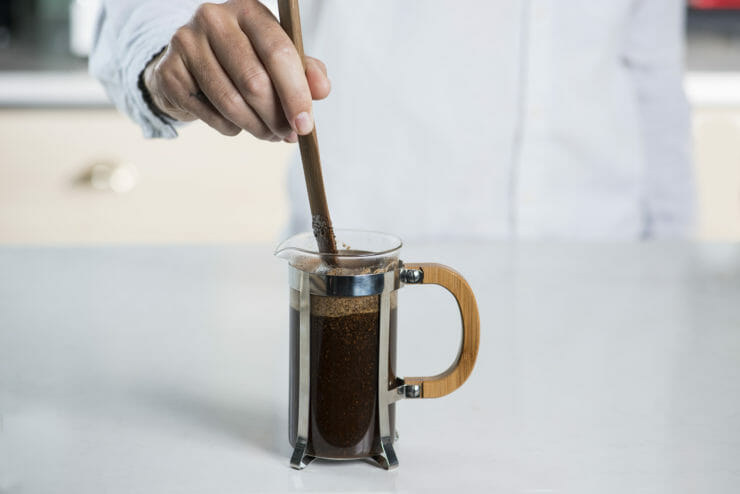 french press filled fully filled with someone stirring the espresso and water. 