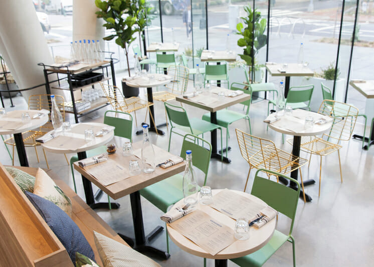 Interior shot of Bluestone Lane West End with the green chairs and white tables.