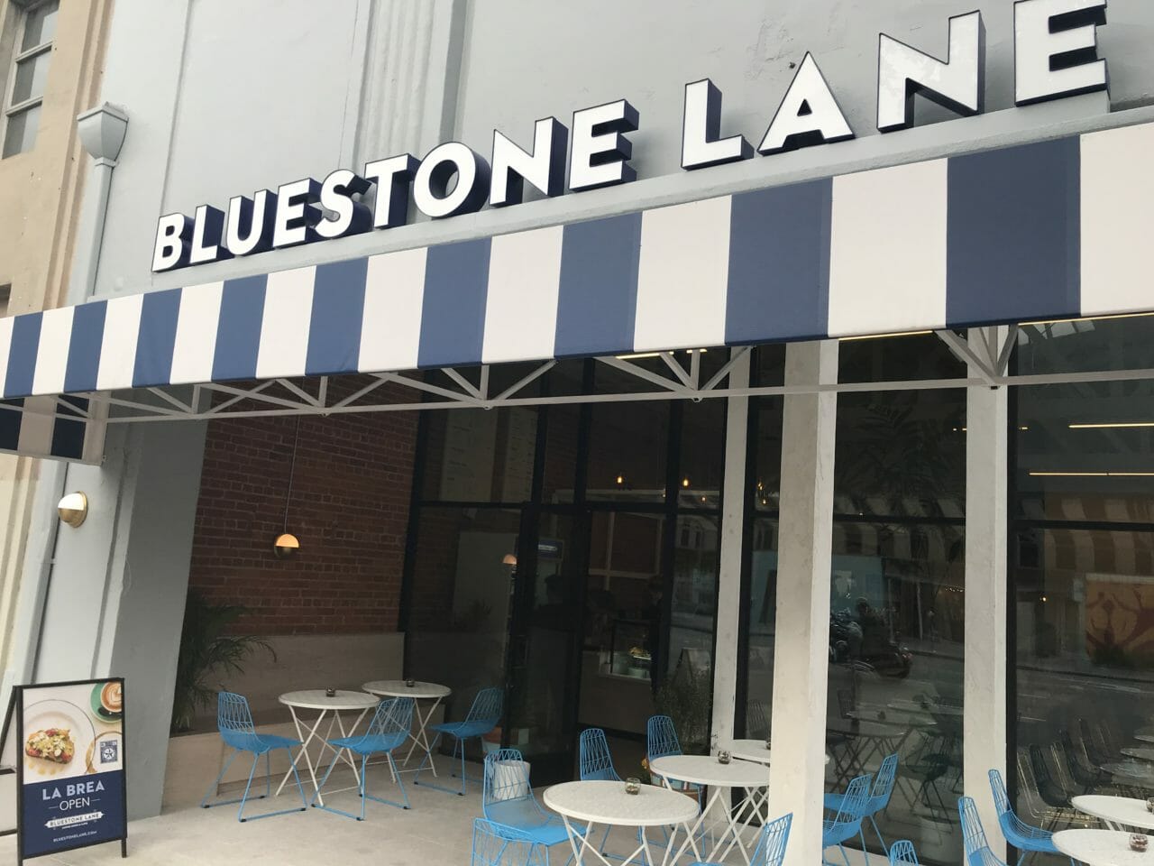 exterior of Bluestone Lane La Brea with blue and white awning.