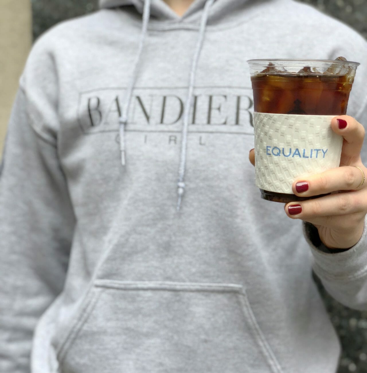 Lady in bandier sweatshirt holding cold brew with equality sleeve
