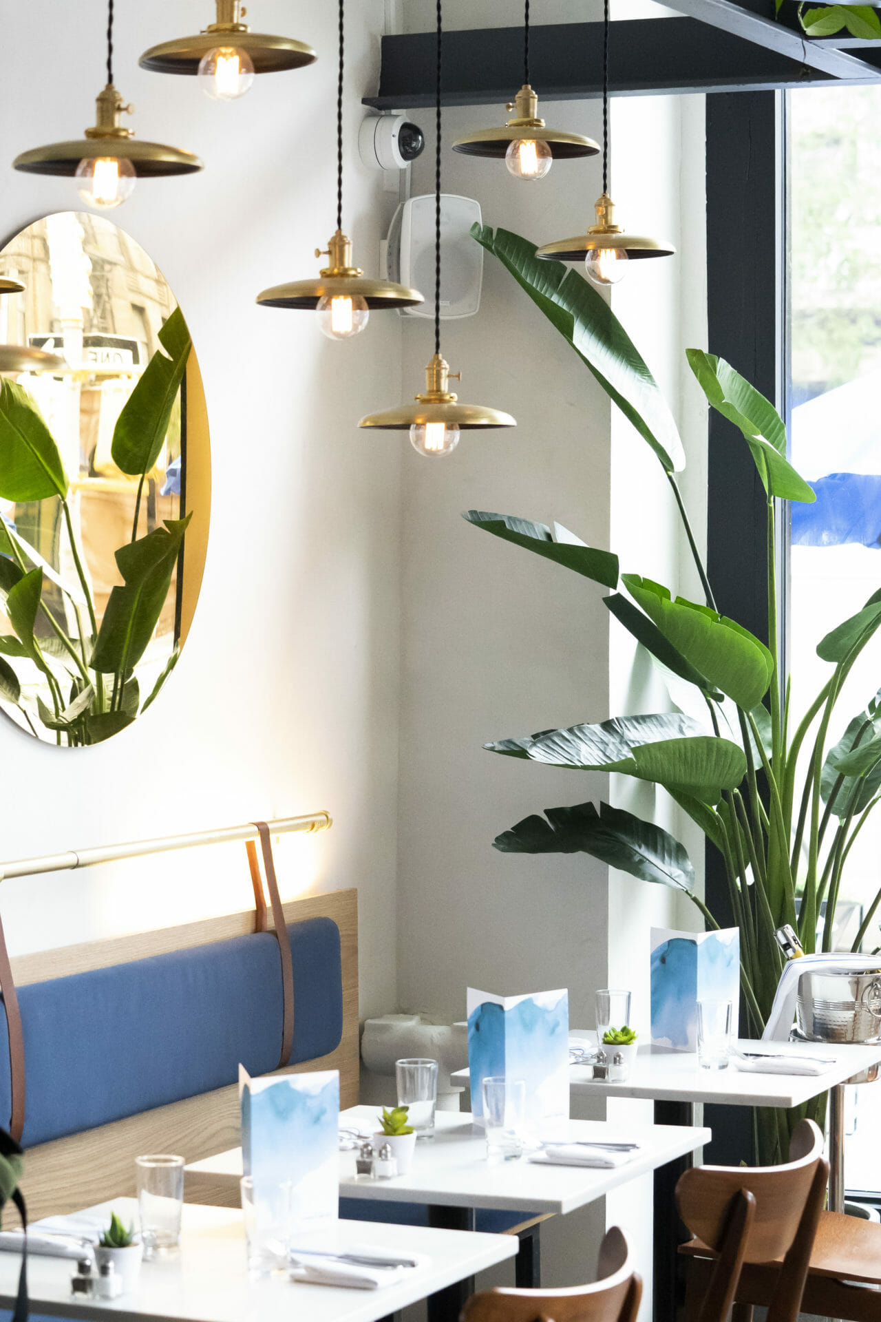 Interior of Upper West Side with a focus on the blue seating area, large green plants and gold hanging mirror.
