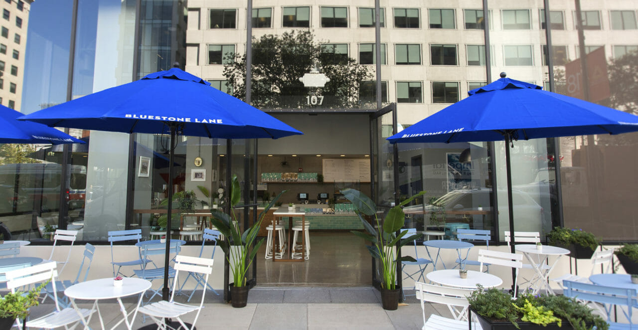 exterior of Bluestone Lane 1150 Connecticut with large blue umbrellas and blue and white table seating outside.