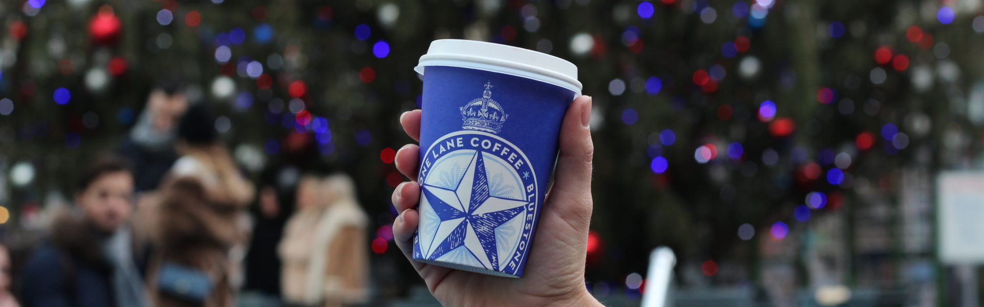 Coffee cup being held up in front of a Christmas tree
