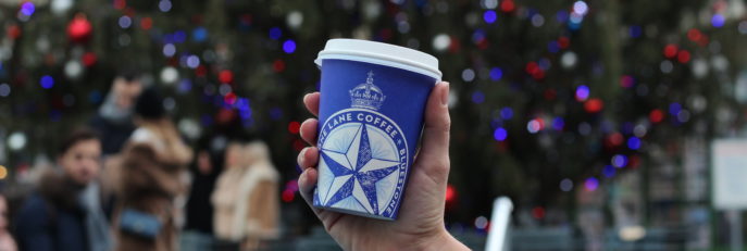 Coffee cup being held up in front of a Christmas tree