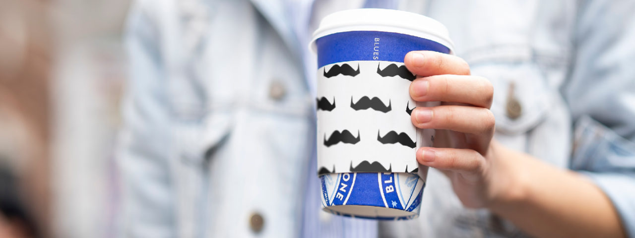 Man holding cup with a sleeve covered in mustaches
