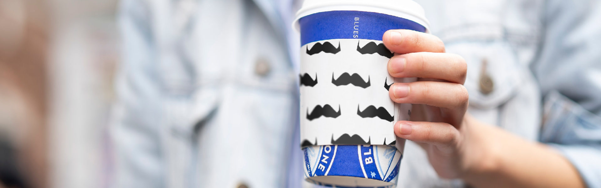 Man holding cup with a sleeve covered in mustaches