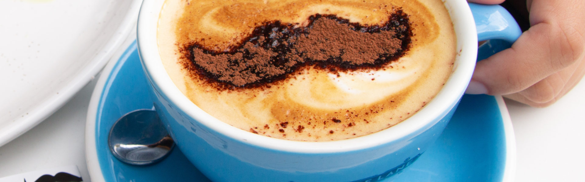 A cup of coffee with a mustache stenciled in chocolate powder