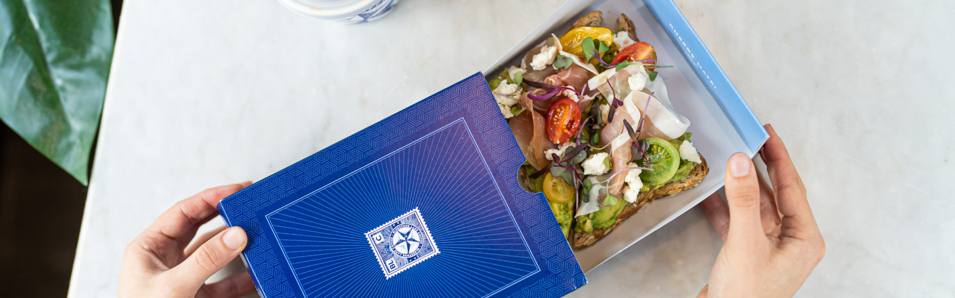 Hands open a Bluestone Lane box with avo smash inside