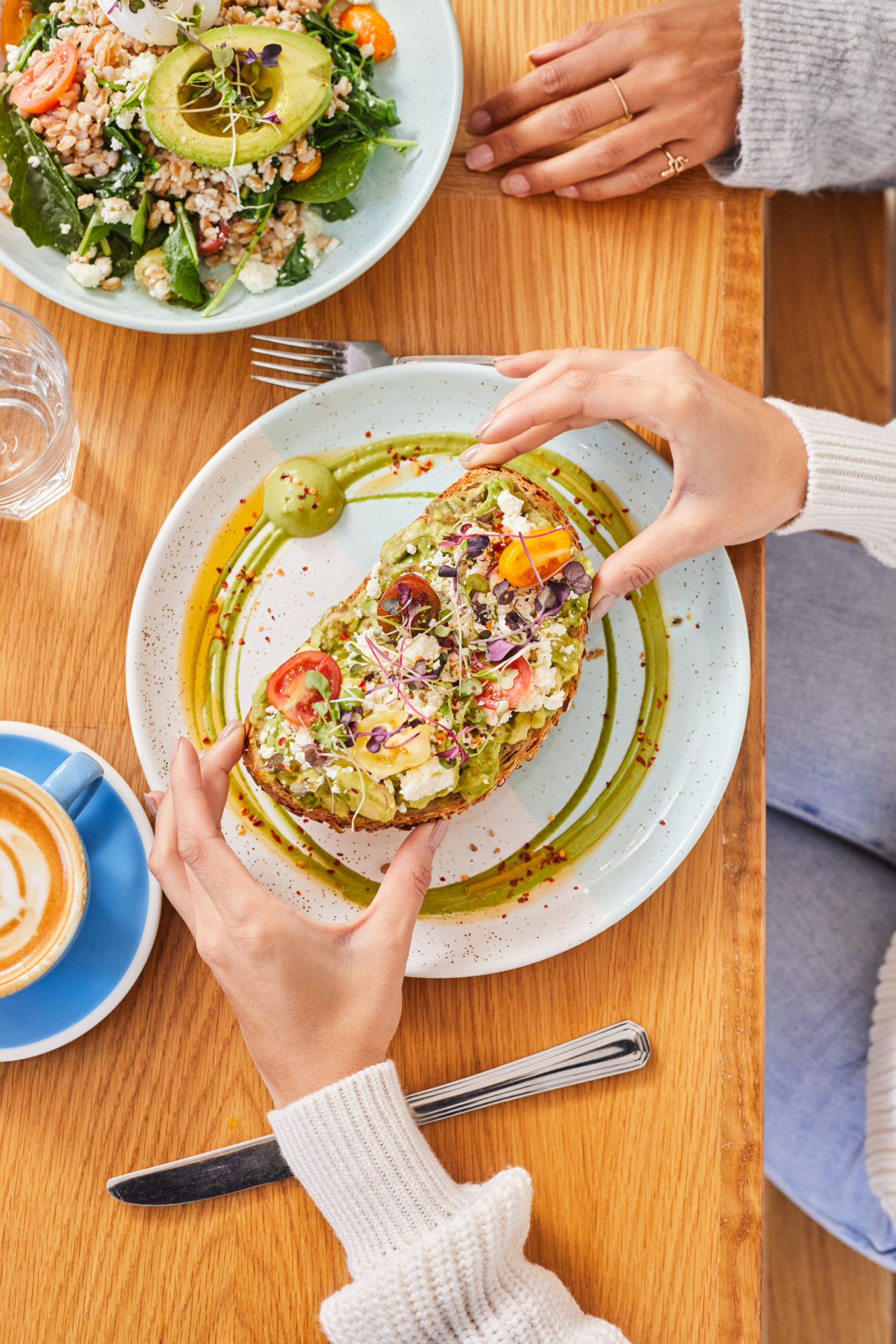 Birds eye view of a woman's hands holding a piece of avocado toast above a plate.