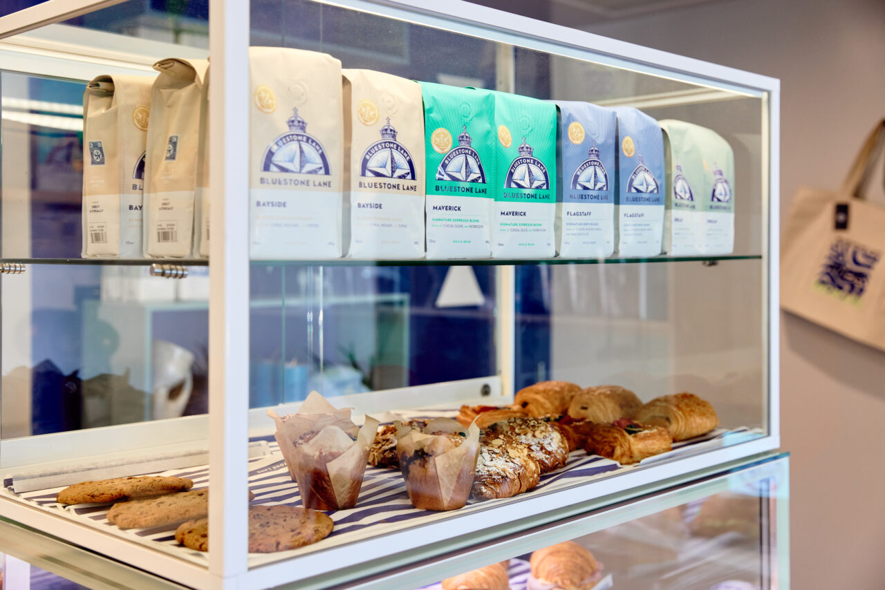 A pastry case containing muffins, pastries and Bluestone Lane coffee bags.