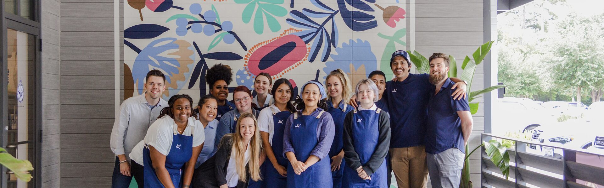 Bluestone Lane teammates stand in front of a mural smiling