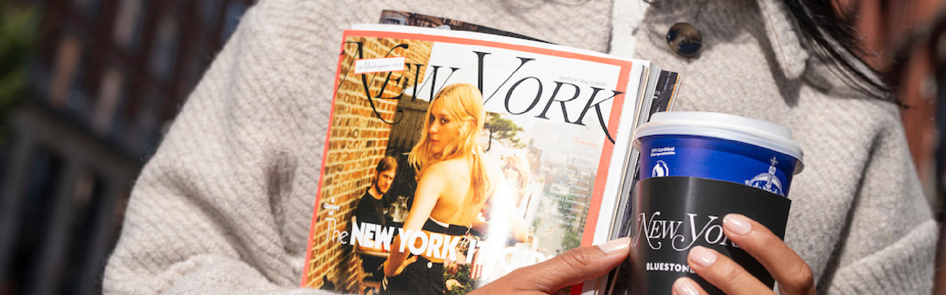 A model holds a New York Mag in one hand and a Bluestone Lane takeaway cup in the other