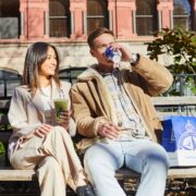 2 people sitting on park bench drinking coffee