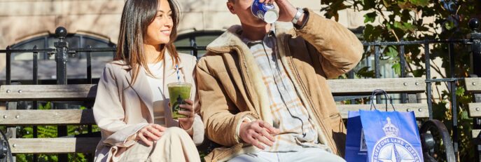 2 people sitting on park bench drinking coffee